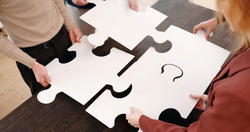 Pöydän ääressä neljä ihmistä sovittaa palapelinpaloja yhteen.