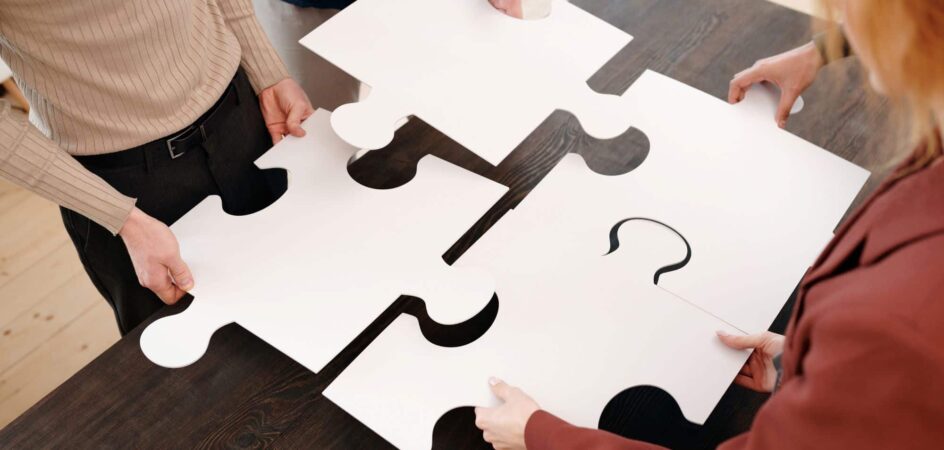 Pöydän ääressä neljä ihmistä sovittaa palapelinpaloja yhteen.