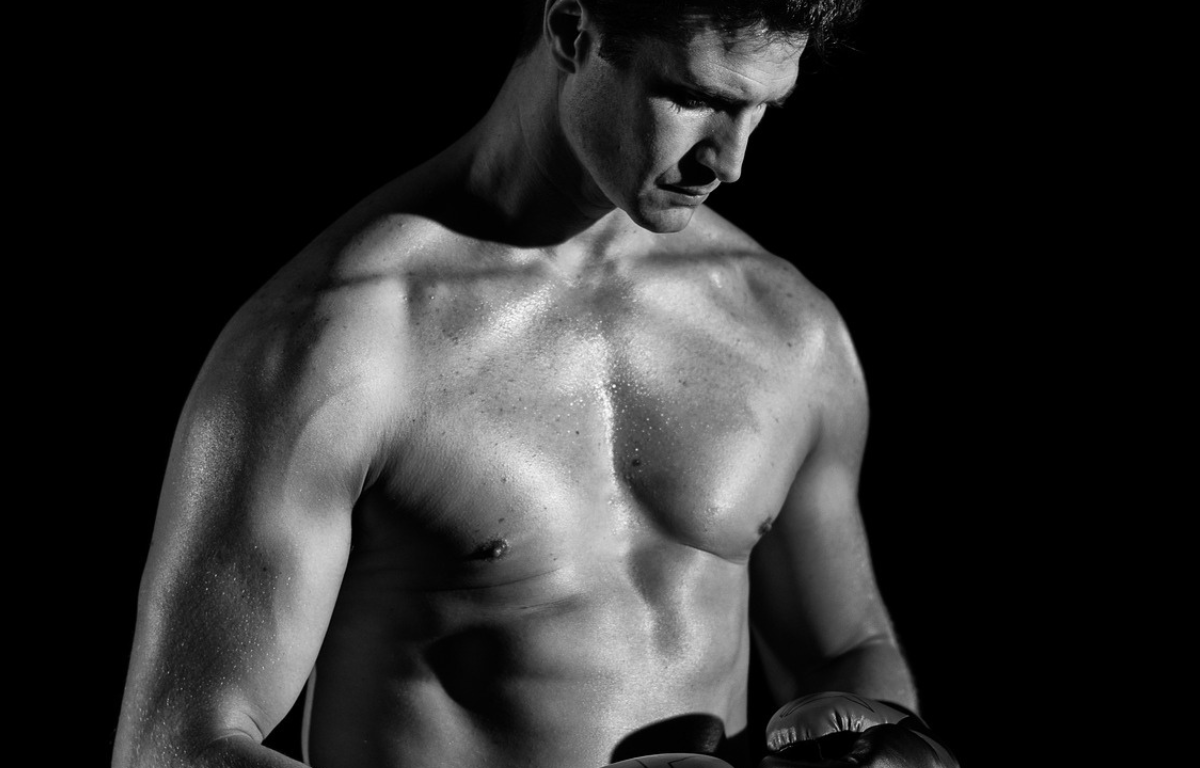 Mustavalkoinen kuva lihaksikkaasta miehestä nyrkkeilyhanskat kädessä