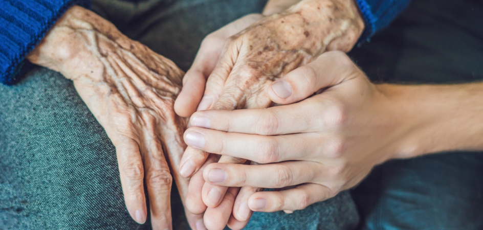 Henkilö pitää kiinni ikääntyneen ihmisen kädestä.