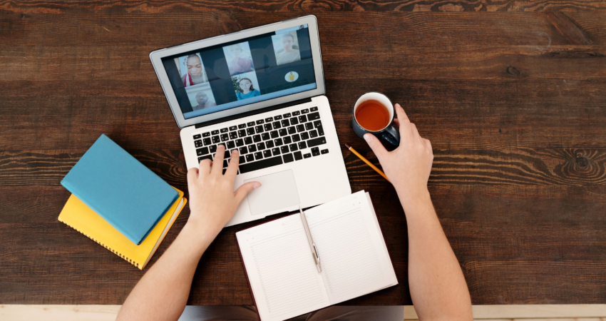 Henkilö tietokoneella kahvikuppi kädessä.