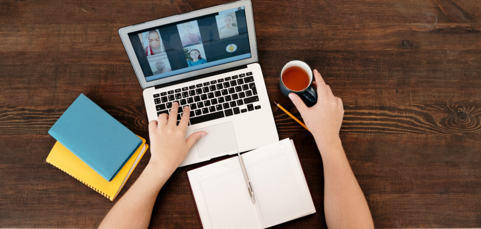 Henkilö tietokoneella kahvikuppi kädessä.