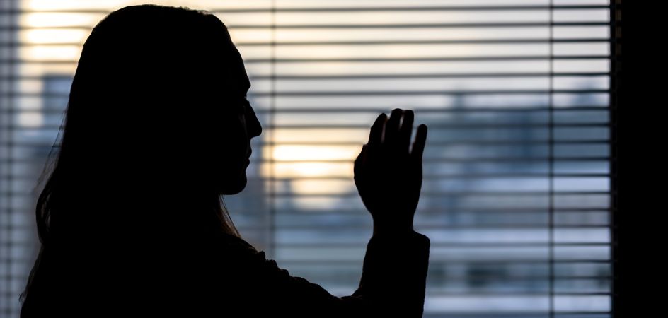 Nuori naisoletettu katsoo ikkunasta ja koskettaa viimeistä auringonsädettä. Silhuettikuva, jossa ei näy kasvoja