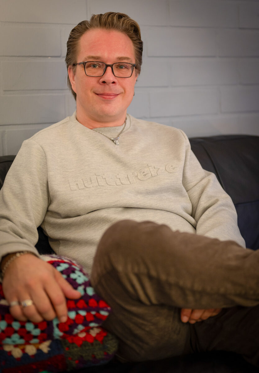 Henkilö istuu sohvalla jalka toisen päällä ja katsoo kameraan