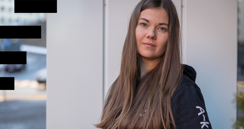 Pitkähiuksinen nainen katsoo kameraan ulkona