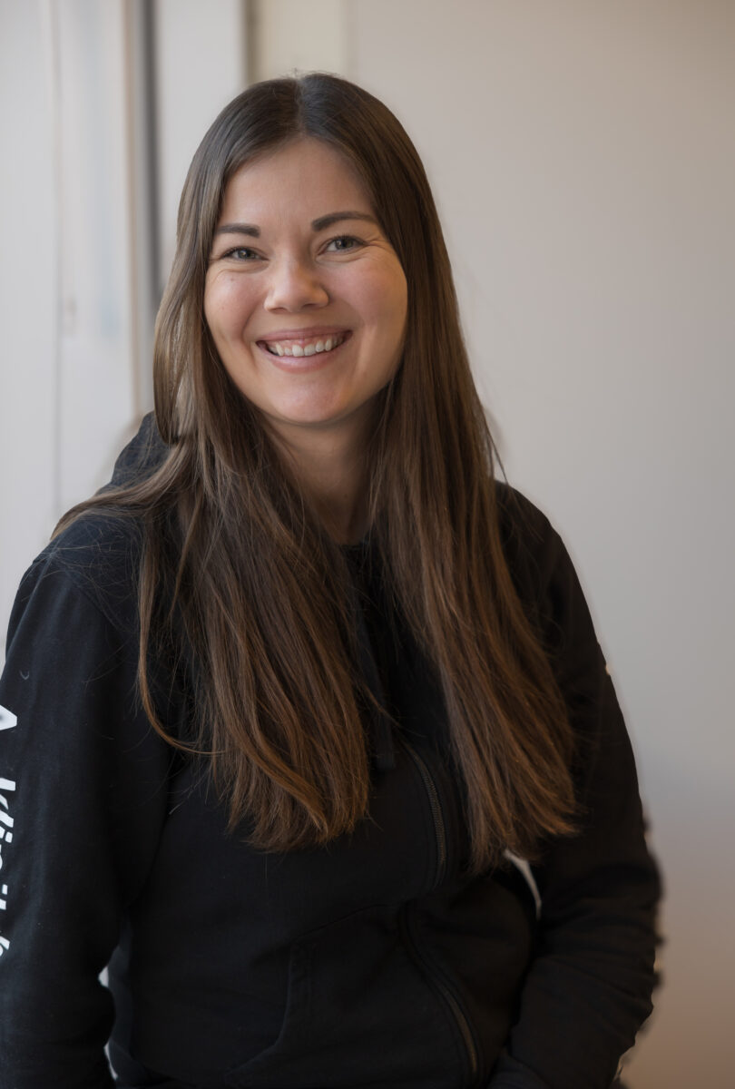 Nainen istuu ikkunalaudalla ja katsoo kameraan sekä hymyilee