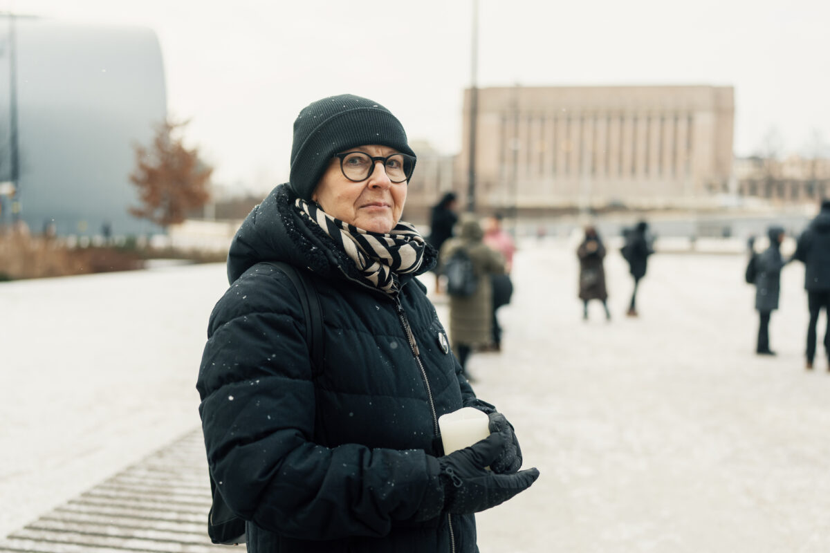 Kuvassa nainen katsoo kameraan ja pitelee kädessään hautakynttilää