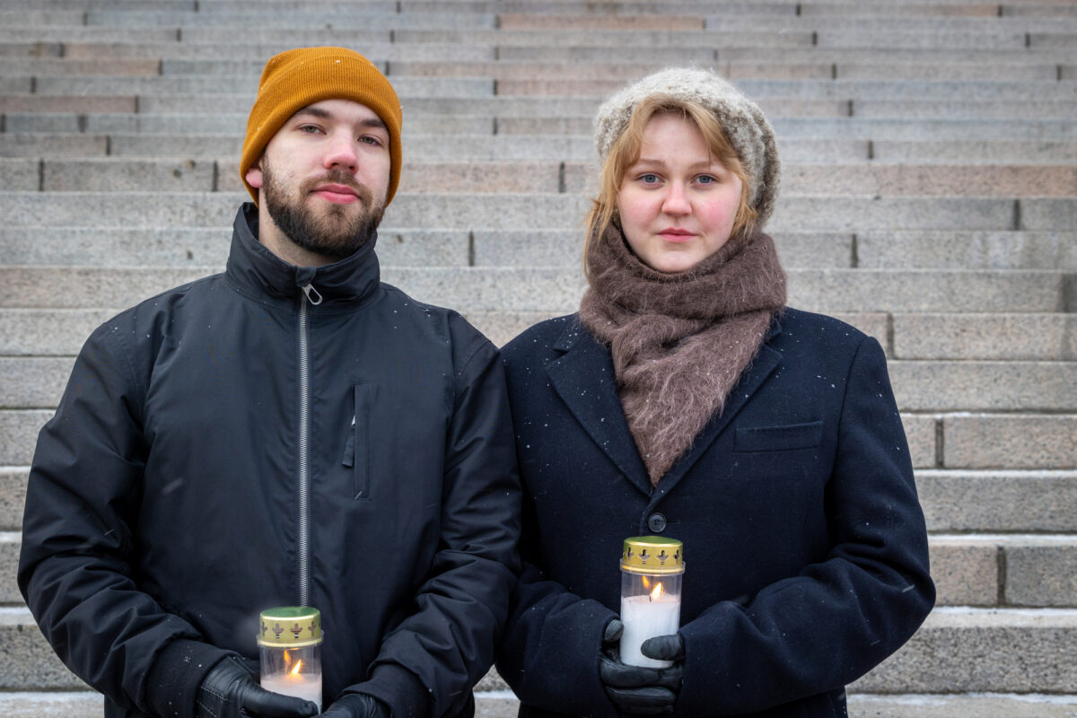 Kuvassa kaksi ihmistä seisoo Eduskuntatalon portailla ja pitelee hautakynttilöitä
