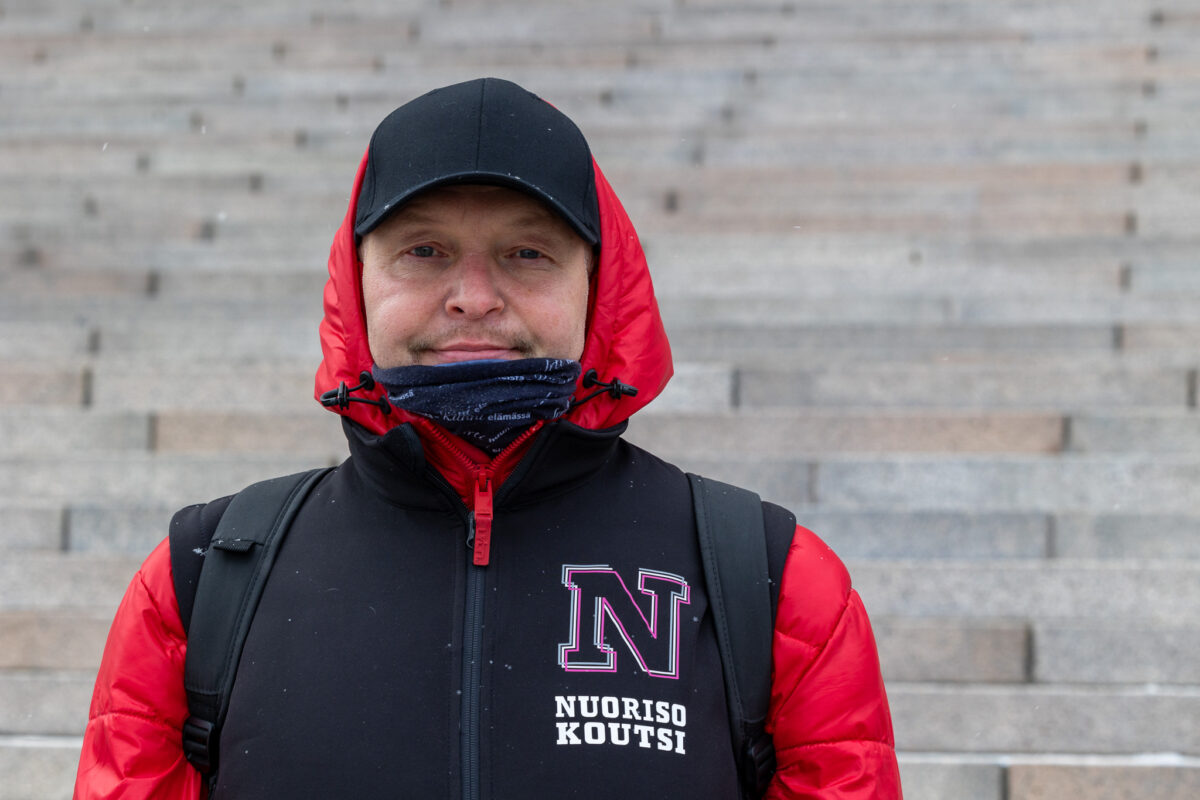 Kuvassa mies seisoo Eduskuntatalon portailla lippahattu päässä