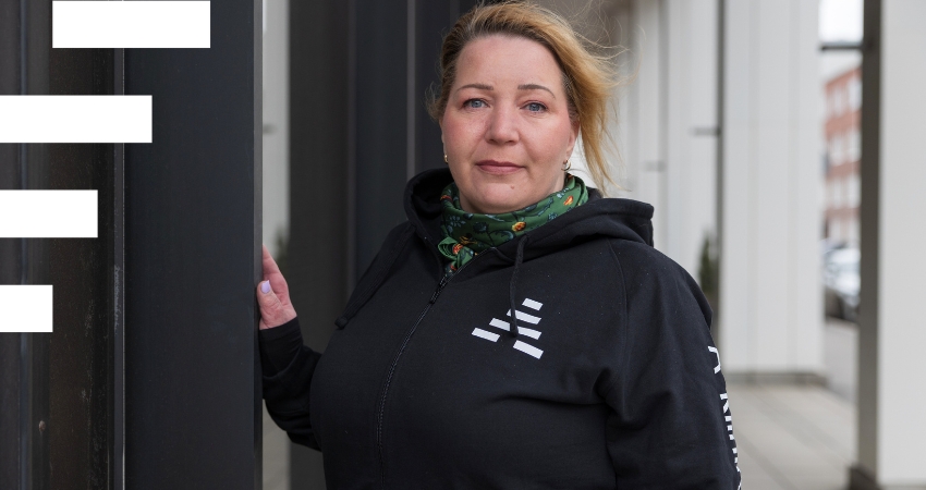 Henkilö katsoo ulkona kameraan. Hänellä on päällään musta huppari, jossa lukee A-klinikkasäätiö