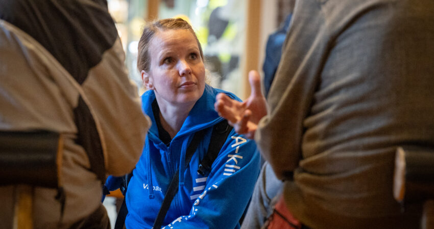 Kuvassa henkilö sinisessä hupparissa keskustelee kahden ihmisen kanssa. Sinisessä hupparissa lukee A-klinikkasäätiö, Vaparit