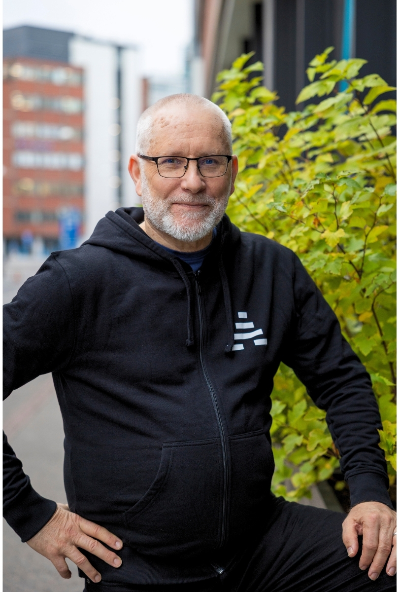 Kuvassa henkilö katsoo kameraan ulkona ja hänellä on yllään musta A-klinikkasäätiön huppari