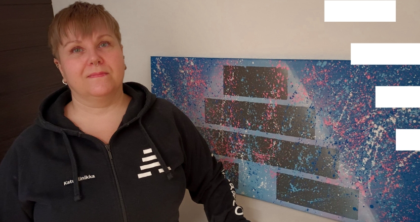 Haittoja vähentävää päihdetyötä tekevä työntekijä seisoo seinällä olevan taideteoksen edessä.