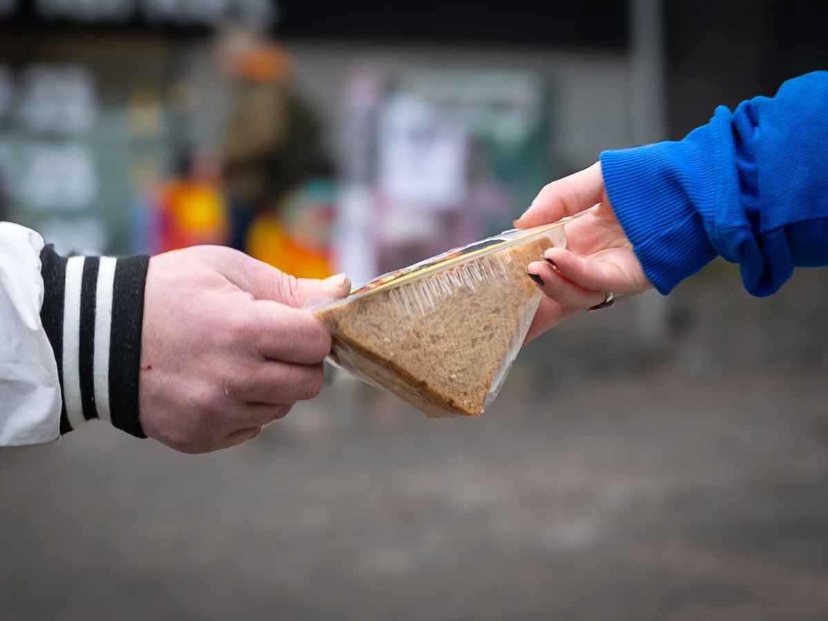 Kuvassa vapaaehtoinen ojentaa apua tarvitsevalle ihmiselle kolmioleivän. Lähikuva heidän käsistään.