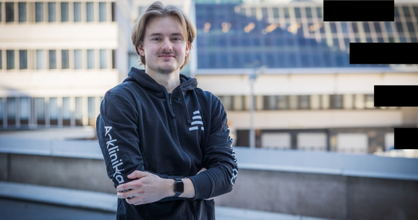 Kuvassa henkilö seisoo kaupunkimaisemassa ja katsoo kameraan. hänellä on yllään musta A-klinikkasäätiön huppari