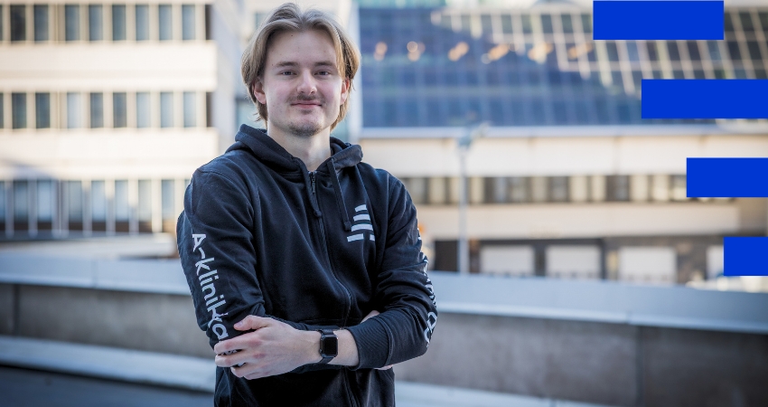 Kuvassa henkilö seisoo kaupunkimaisemassa ja katsoo kameraan. hänellä on yllään musta A-klinikkasäätiön huppari