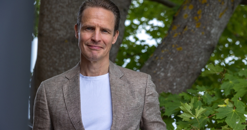 Kuvassa A-klinikkasäätiön toimitusjohtaja Hannu Jouhki katsoo kameraan. Hänellä on yllään ruskea pikkutakki ja valkoinen paita