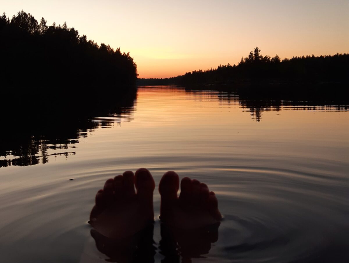 Tyyni järvi, auringonlasku, varpaat näkyvissä veden pinnalla