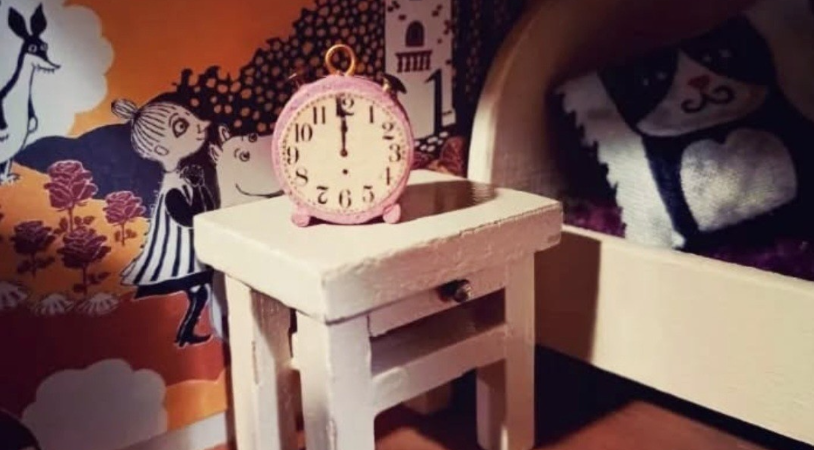 nukkekodin huone, jossa sänky, yöpöytä ja herätyskello