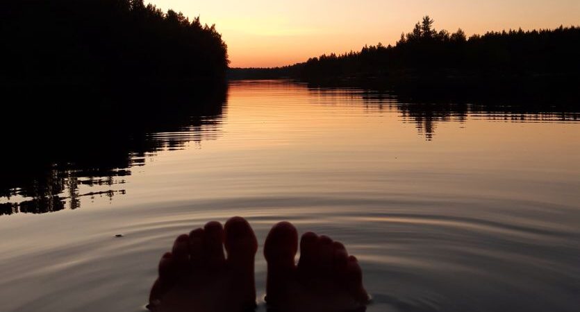 Auringonlasku järvellä, vain varpaat näkyvät tyynen vedenpinnan päällä