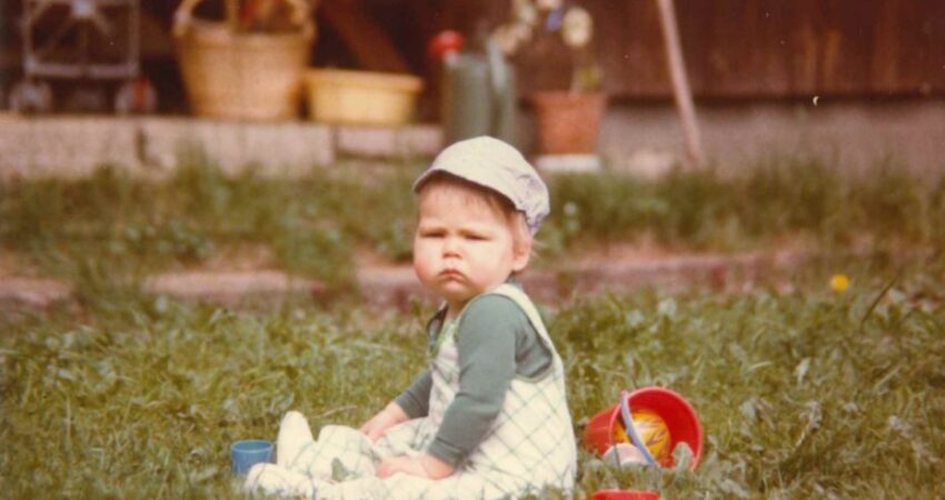 Pieni lapsi istuu kulmat kurtussa nurmikolla lelujen keskellä