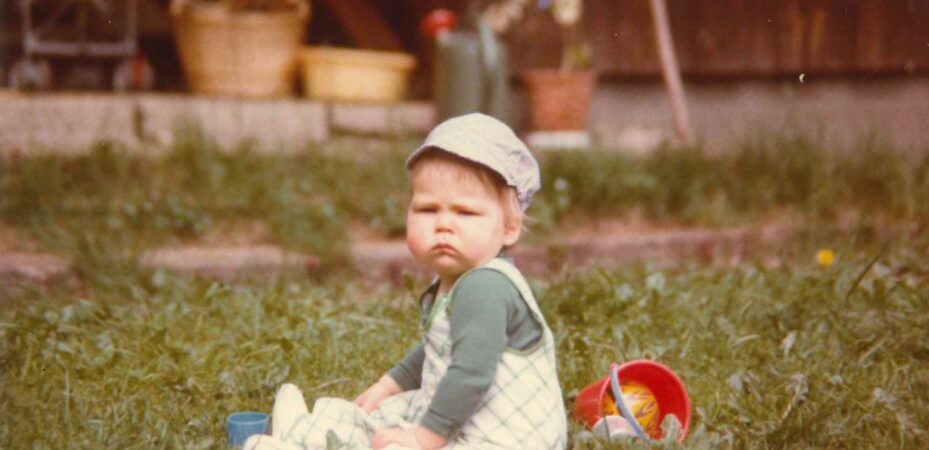 Pieni lapsi istuu kulmat kurtussa nurmikolla lelujen keskellä