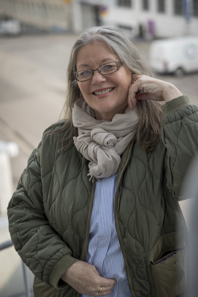 Marjo nojaa portaiden kaiteeseen ja hymyilee rennosti